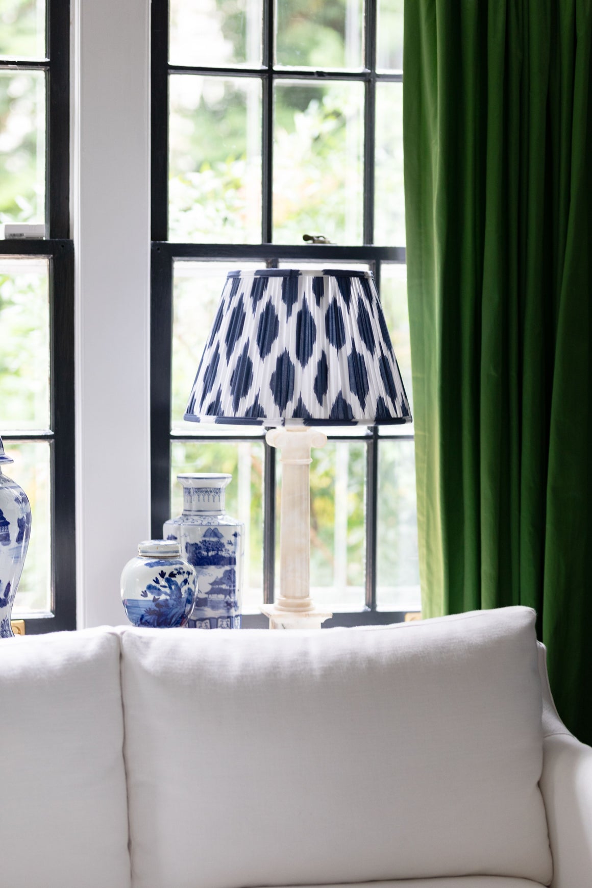 Blue lamp shade in front of green curtains. 